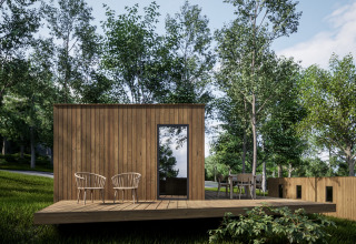 Modern wooden cabin with deck and chairs surrounded by trees at Hameau de l'Ourthe holiday park, Belgium.