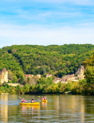 Mensen kanoën op een rivier nabij Saint Cybranet, omringd door groene heuvels en landelijke huisjes.