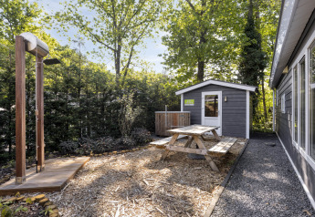 Haveområde ved Wellness Lodge på De Thijmse Berg med træbord, udendørs bruser og lille skur omgivet af træer.