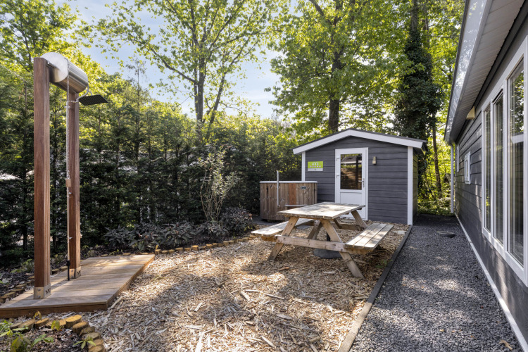 Gartenbereich der Wellness Lodge auf De Thijmse Berg mit Sitzbank, Außendusche und Schuppen im Grünen.