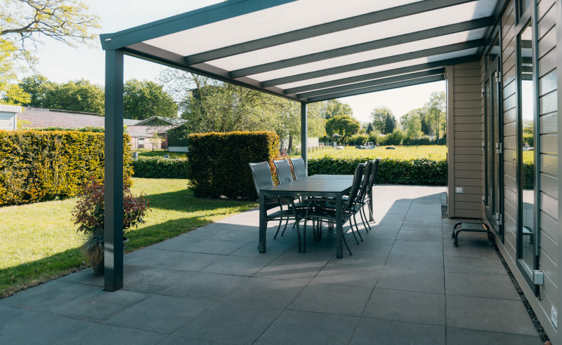 Covered patio at Veluwe Villa, Holiday park De Boshoek in the Netherlands, featuring a garden and dining table.