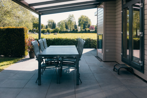 Overdekt terras met eetset aan Veluwe Villa in vakantiepark De Boshoek, Nederland, met uitzicht op weiland.