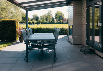 Overdekt terras met eettafel en stoelen bij Veluwe Villa, vakantiepark De Boshoek, Nederland.