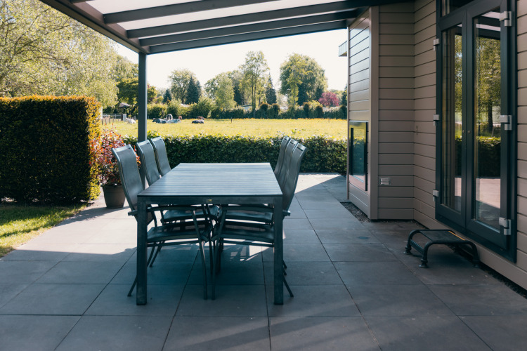 Covered patio with dining table and chairs overlooking a field at Veluwe Villa, Holiday Park De Boshoek, Netherlands.