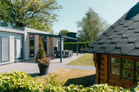 Veluwe Villa lodge bij Holiday park De Boshoek in Nederland, met terras, tuin en houten chalet op de voorgrond.