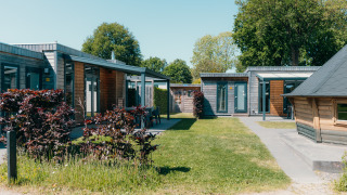 Outdoor view of the Veluwe Villa + sauna at Holiday park De Boshoek, Netherlands, with modern lodges and grass.