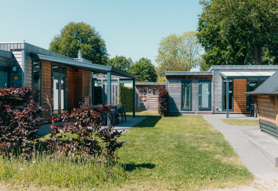 Outdoor view of the Veluwe Villa + sauna at Holiday park De Boshoek, Netherlands, with modern lodges and grass.
