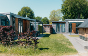 Buitenaanzicht van Veluwe Villa met sauna bij vakantiepark De Boshoek in Nederland, moderne lodges en grasveld.