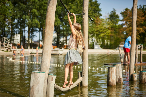 Niña jugando en un curso de obstáculos sobre el agua en De Leistert, parque vacacional en Limburg, Países Bajos.