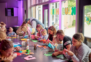 Kinderen en volwassenen knutselen samen aan tafel op De Leistert vakantiepark in Limburg, Nederland.