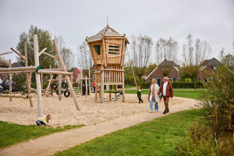 Familien genießen den Spielplatz mit Sand und Holzspielhaus im Ferienpark De Leistert, Limburg, Niederlande.