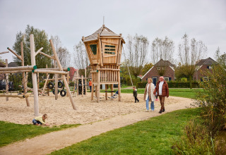 Gezinnen genieten van een zandige speeltuin met houten toestel in De Leistert vakantiepark, Limburg, Nederland.