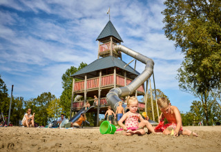 Kinderen spelen in het zand voor een grote speeltoren met glijbaan bij het vakantiepark De Leistert.