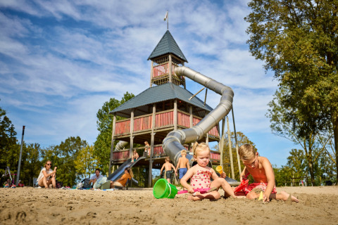 Kinderen spelen in het zand voor een grote speeltoren met glijbaan bij het vakantiepark De Leistert.