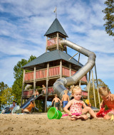 Kinderen spelen in het zand voor een grote speeltoren met glijbaan bij het vakantiepark De Leistert.