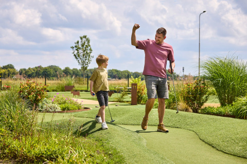 Vader en zoon spelen minigolf in vakantiepark De Leistert in Limburg, Nederland, op een zonnige dag.