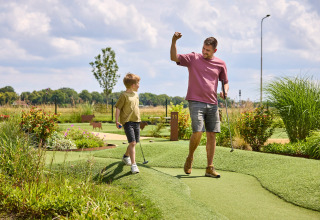 Father and son play mini-golf at De Leistert holiday park in Limburg, Netherlands, on a sunny day.