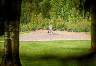 Enfant avec trottinette sur butte de gravier et pneus à De Leistert, parc de vacances, Limbourg, Pays-Bas.