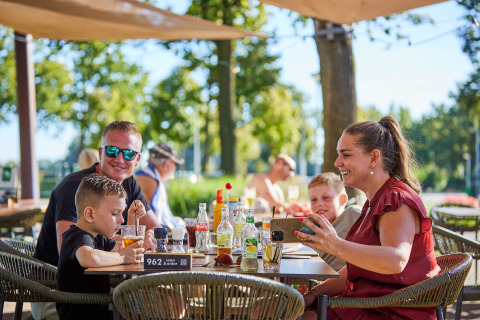 Familie genießt Mittagessen im Freien im Ferienpark De Leistert in Limburg, Niederlande, bei Sonnenschein.
