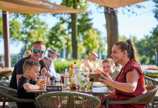 Gezin geniet van een maaltijd op het terras van De Leistert vakantiepark in Limburg, Nederland, bij mooi weer.