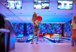 Two children enjoy bowling in a vibrant, neon-lit alley at De Leistert holiday park in Limburg, Netherlands.