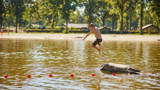 Dreng springer fra sten i lavvandet sø ved stranden i ferieparken De Leistert i Limburg, Holland.