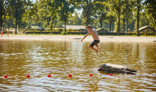 Jongen springt van een steen in het water in vakantiepark De Leistert, Limburg, Nederland.