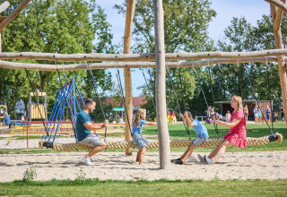 A family enjoys a large rope swing together at the playground in De Leistert holiday park, Limburg, Netherlands.