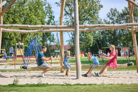 Familie spielt gemeinsam auf einer großen Seilschaukel auf dem Spielplatz im Ferienpark De Leistert, Limburg.