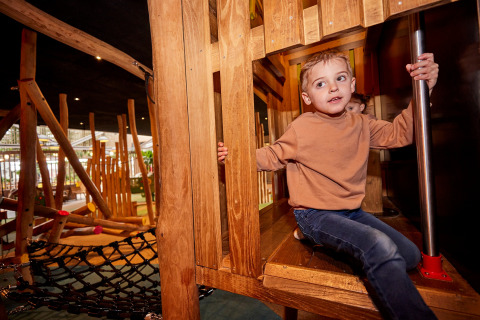 Jongen speelt op houten speeltoestel in vakantiepark De Leistert, Limburg, Nederland, tussen houten balken.