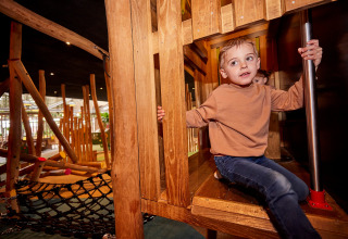 Boy playing on a wooden playground at De Leistert holiday park in Limburg, Netherlands, surrounded by beams.