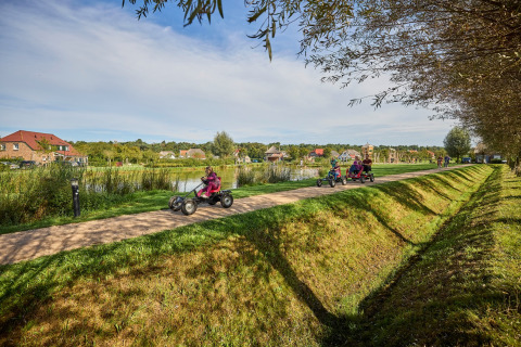 Vakantiepark De Leistert in Limburg, Nederland, met gezinnen op skelters langs een pad bij het water.