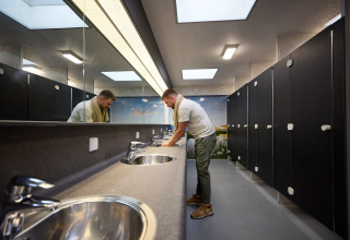 Man washing hands in a modern restroom at De Leistert holiday park in Limburg, Netherlands, with stalls.