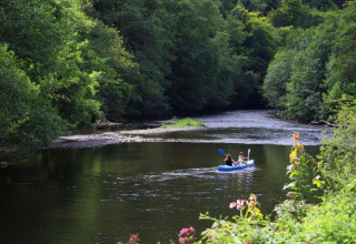 Two people kayaking on a calm river surrounded by green forest at a holiday park with glamping sites.