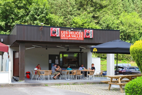 Outdoor seating at Les Délices de la Vallée restaurant in a holiday park, surrounded by lush greenery.
