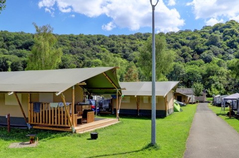 Glamping-tenten op een vakantiedomein, tussen groene heuvels, bomen en een heldere blauwe lucht.