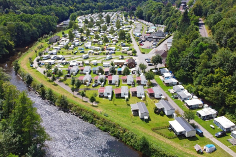 Vista aerea di un villaggio turistico con glamping, bungalow e un fiume circondato dal verde.