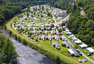 Vista aérea de un parque vacacional con alojamientos glamping y cabañas junto a un río boscoso.