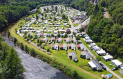 Aerial view of a holiday park featuring glamping accommodations, cabins, and riverside greenery.