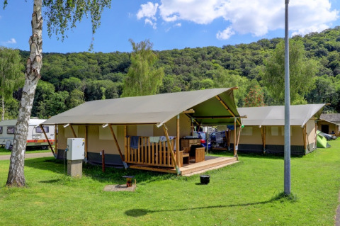 Glampingverblijven in een vakantiepark met canvas tenten en een groene, heuvelachtige achtergrond.