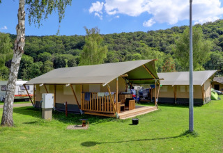 Glamping-Unterkünfte in einem Ferienpark, große Zelte auf einer Wiese mit bewaldeten Hügeln dahinter.