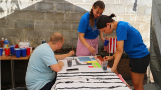 Drei Personen malen gemeinsam an einem großen Leinwandtuch in einem Ferienpark mit Glamping-Angebot.