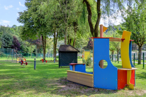 Spielplatz mit bunten Spielgeräten im Grünen, gelegen in einem Ferienpark mit Glamping-Unterkünften.