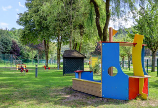 Legeplads med farverigt legetøj og legeredskaber i en grøn feriepark med glamping faciliteter.