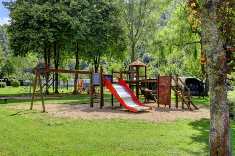 Speeltuin in een vakantiepark met glamping-verblijven, omgeven door groen en bomen.