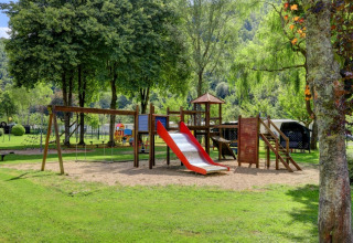 Playground at a holiday park featuring glamping accommodations, surrounded by lush trees and grass.