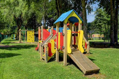 Parco giochi colorato in un villaggio vacanze con glamping, circondato da alberi e prato verde.