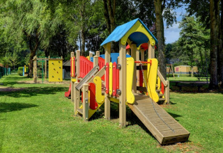Parco giochi colorato in un villaggio vacanze con glamping, circondato da alberi e prato verde.