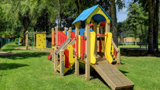 Spielplatz mit buntem Klettergerüst in einem Ferienpark mit Glamping-Unterkünften und viel Grün.