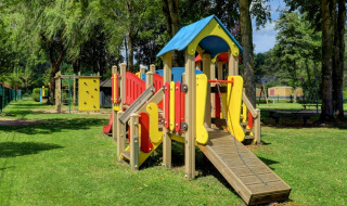 Spielplatz mit buntem Klettergerüst in einem Ferienpark mit Glamping-Unterkünften und viel Grün.
